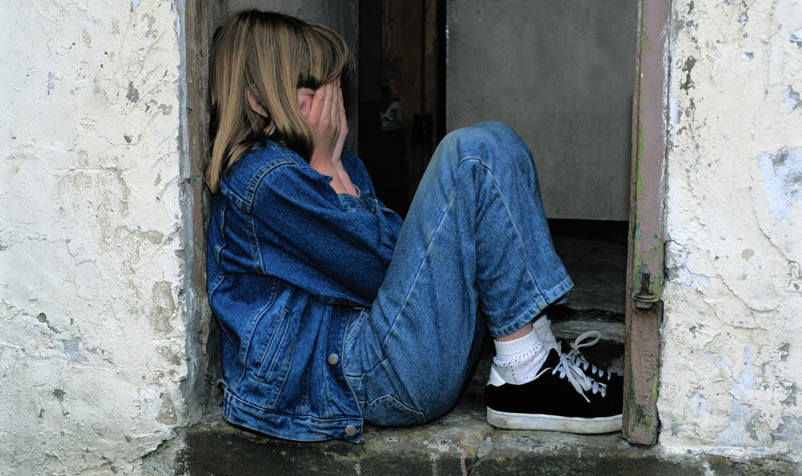 A girl wearing denim crying while covering her face