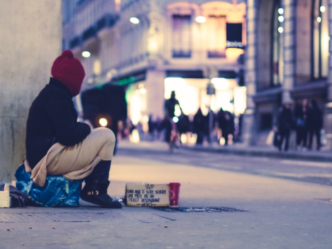 A homeless person sitting on the side of a road with a sign