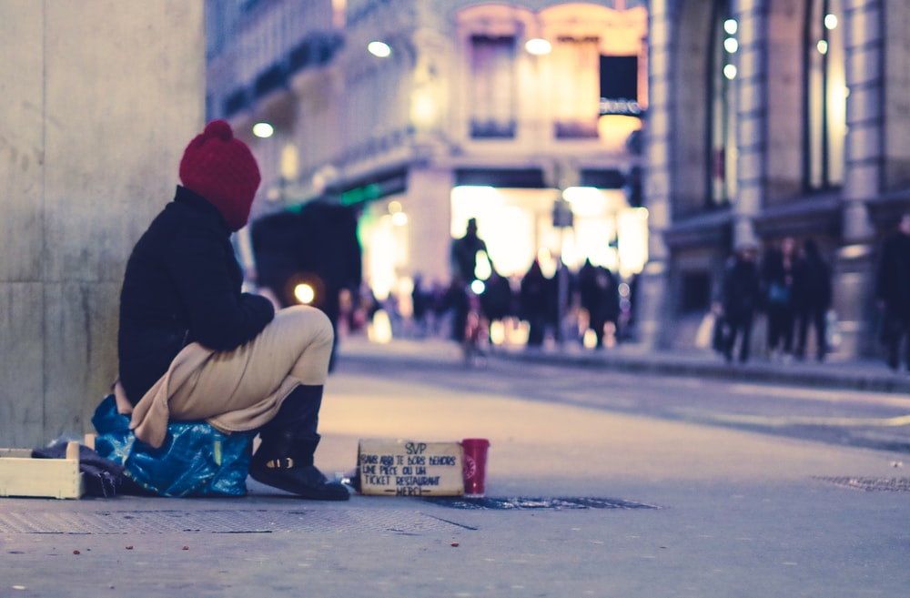 A homeless person sitting on the side of a road with a sign