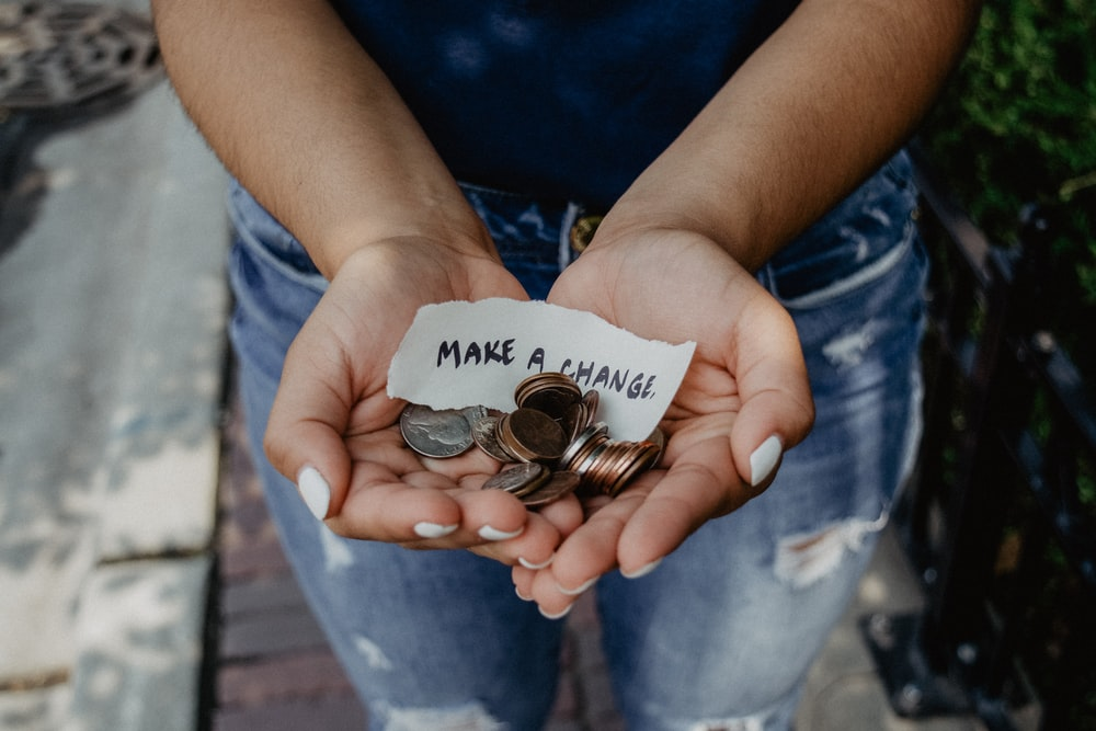 A person holding coins and a note that says “Make a Change” in their hands